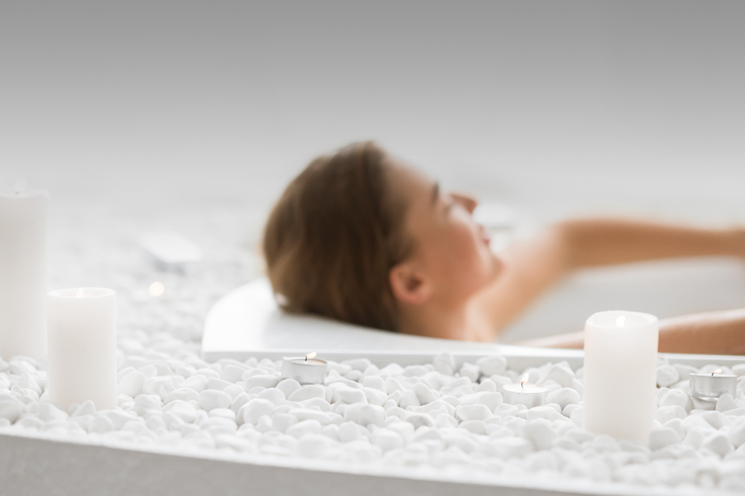 Woman reclines in a bathtub with candles nearby