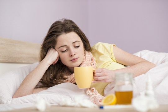 Sick woman lying in bed with high fever. She has cold and flu. She is drinking tea with honey and lemon.